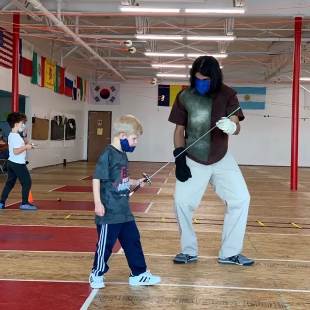 A coach guiding a young fencer through an early lesson