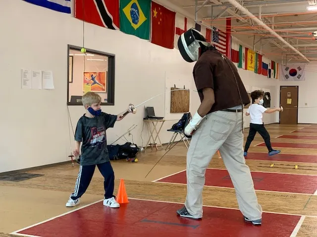A young fencer and coach practicing together on the strip